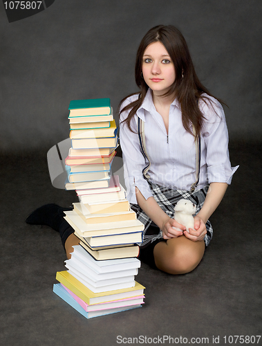 Image of The beautiful schoolgirl sits near a pile of books