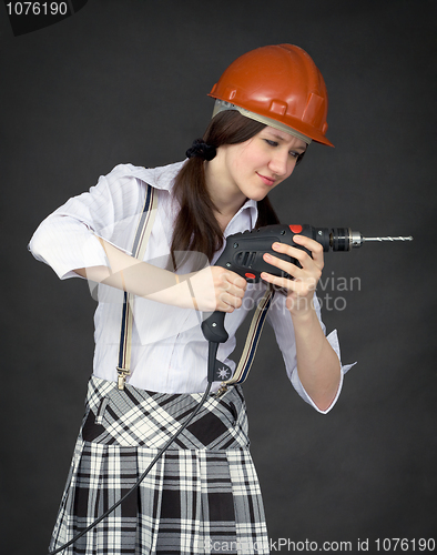 Image of Girl in a helmet learns to use a drill