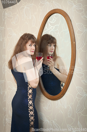 Image of Beautiful young girl standing near a mirror with wine glass in h