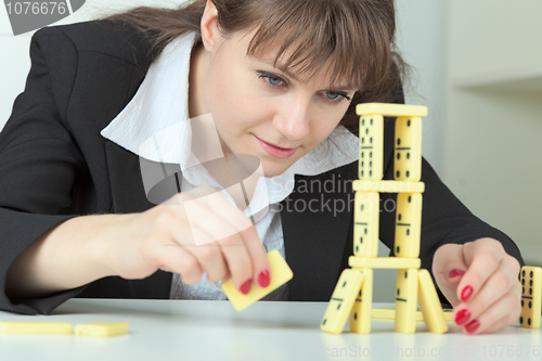 Image of Young woman builds tower of dominoes bones on table