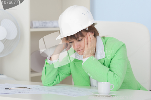 Image of Woman - engineer in protective helmet sits at table on workplace