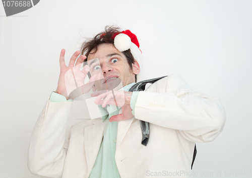 Image of Amusing man in white suit and christmas cap is frightened