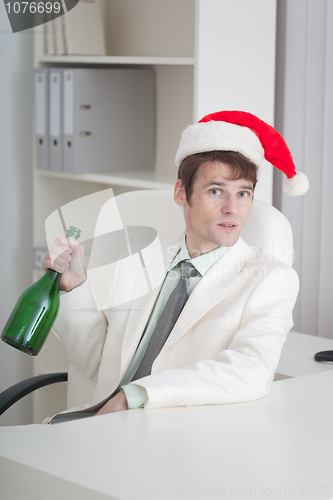 Image of Young man in Christmas cap sits with bottle at table