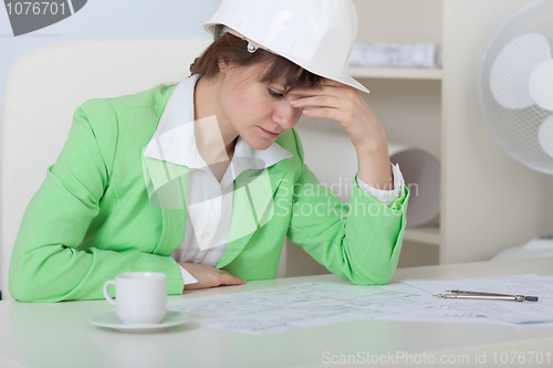 Image of Tired woman - engineer in helmet sits at table in office