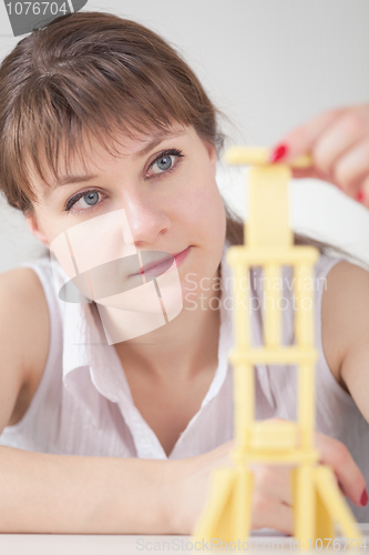 Image of Young girl concentrated builds on table tower of dominoes