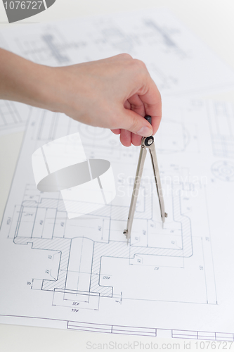 Image of Hand holds metal compasses against drawings