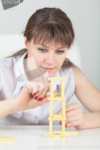 Image of Young girl builds tower of dominoes bones on table