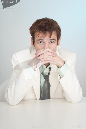 Image of Young sorrowful person in white suit sits at table