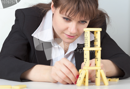 Image of Young girl in black concentrated builds tower of dominoes