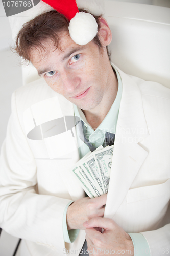 Image of Businessman in white suit and Christmas cap hides money in pocke