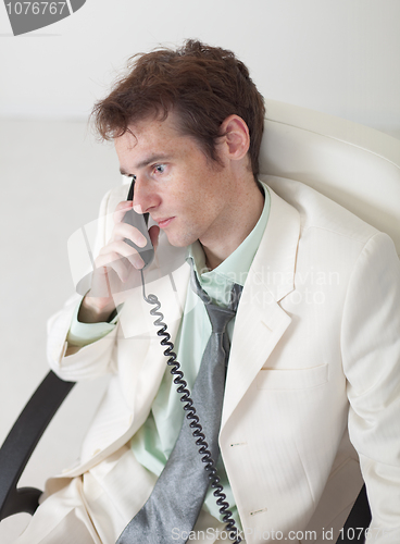 Image of Man in white suit speaks by phone sitting in an armchair