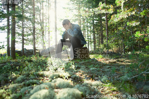 Image of Sad young man sits in wood on stone