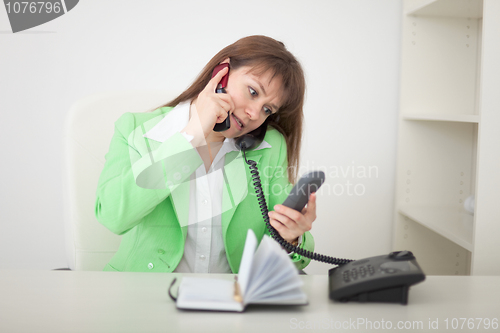 Image of Girl at office talks by several phones simultaneously
