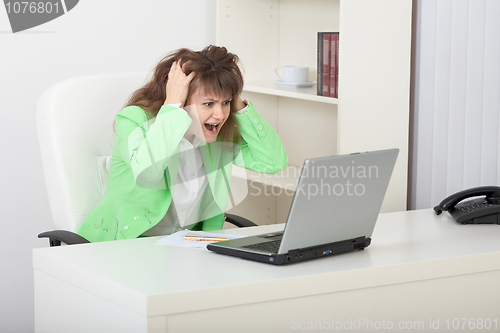 Image of Emotional young woman on workplace with laptop
