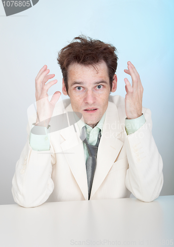 Image of Young sorrowful man in white suit sits at table