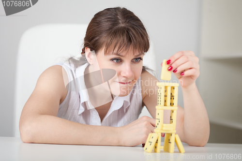 Image of Beautiful young woman builds tower of dominoes