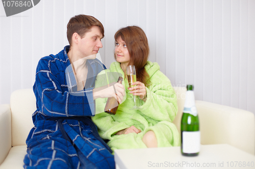 Image of Young pair at home on divan with beer and wine