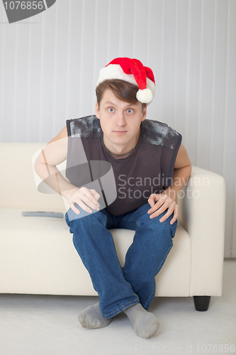 Image of Guy in Christmas cap sits on sofa having stare wide-eyed