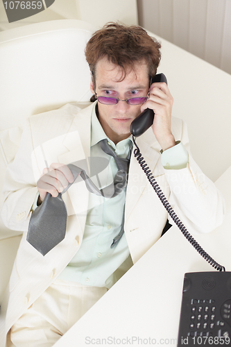 Image of Young businessman speaks on phone, worries and rumples tie