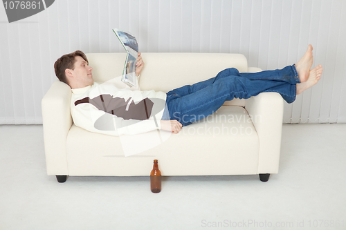 Image of Person comfortably lie on sofa with beer and journal