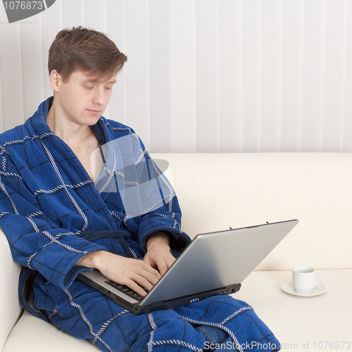 Image of Young man in dressing gown with laptop