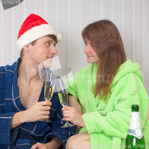 Image of Young pair drinks champagne sitting on sofa in dressing gowns