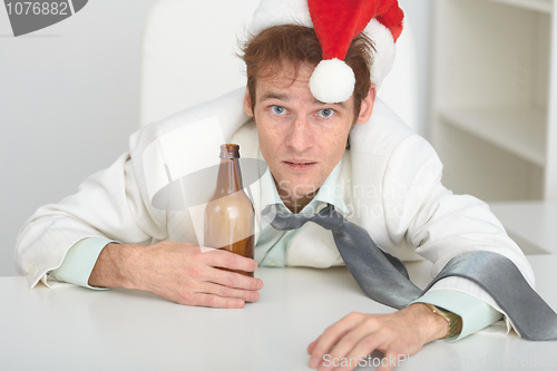 Image of Young man in Christmas hat at office with a beer bottle