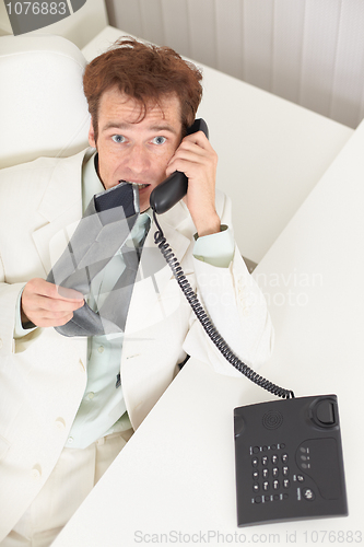 Image of Young businessman speaks on phone, worries and bites tie