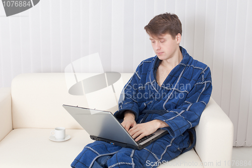 Image of Young man works with laptop in blue dressing gown