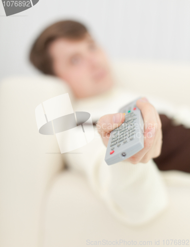 Image of Man lying on sofa uses remote control