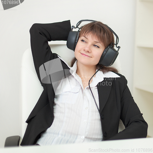 Image of Young girl with big professional ear-phones on head sits in an a