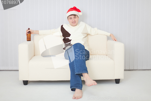 Image of Person in a Christmas cap comfortably sits on sofa with beer
