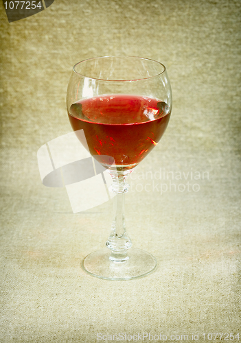 Image of One glass with red wine against brown drapery