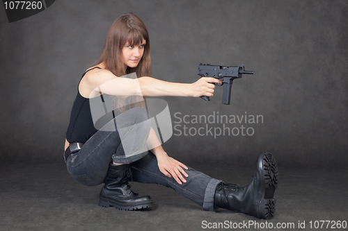 Image of Young woman shoots from pistol sitting on one leg