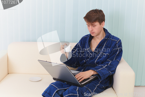 Image of Guy works in Internet on sofa and drinks coffee