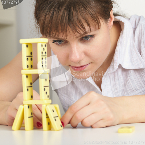 Image of Young woman accurately builds tower of dominoes