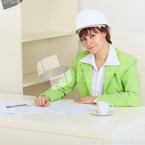 Image of Girl in protective helmet sits at table at office