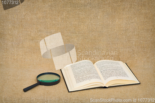 Image of Magnifier and open book lie against a brown canvas