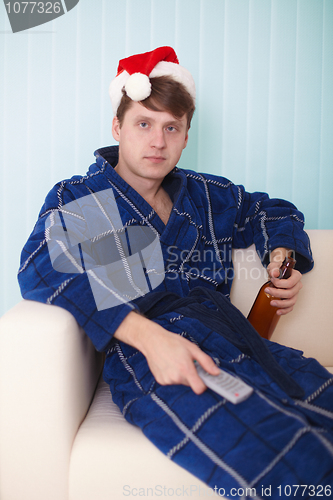Image of person in christmas hat sits on sofa with beer