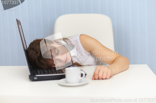Image of Young woman sleeps on laptop keyboard on workplace
