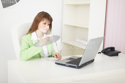 Image of Young woman sits at table at light office with laptop