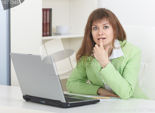 Image of Young woman sits at table at light office with laptop