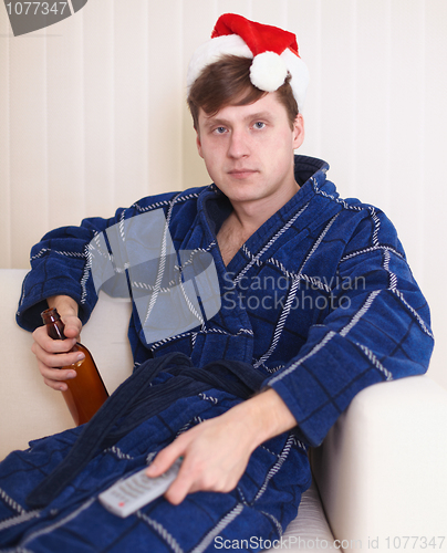Image of Person in christmas hat sits on sofa with beer