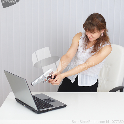 Image of Young woman shoots at laptop from pistol