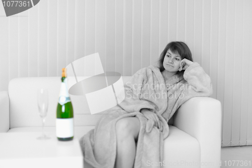 Image of Lonely young woman sits on sofa and looks at wine bottle
