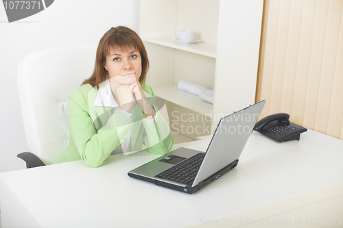 Image of Young woman with laptop sits at table at light office