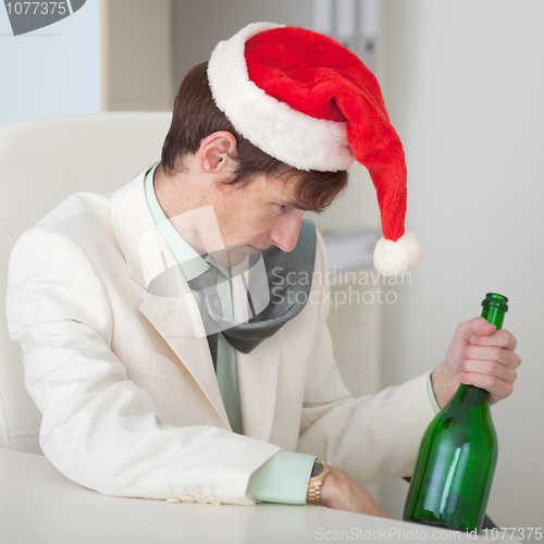 Image of Drunk man in a Christmas cap with bottle sits at table