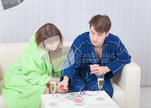Image of Guy and girl play cards on money at home