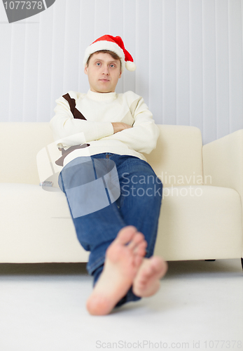 Image of Person in a Christmas cap sits on sofa and watches TV