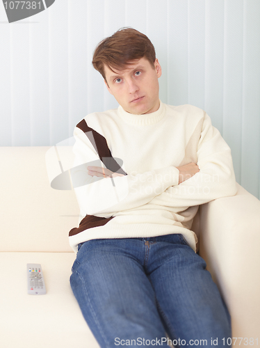 Image of Serious guy sits on sofa with remote control